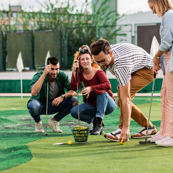 Group of smiling friends enjoying together playing mini golf in the city.